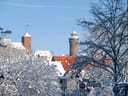 Verschneite Stadtansicht mit Türmen und Bäumen im Winter.