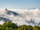 Schloss und Hügel im Nebel mit grüner Baumlandschaft.