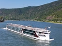 Kreuzfahrtschiff auf einem Fluss vor bewaldeten Hügeln.