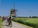 Radfahrergruppe auf Landstrasse mit Windmühle im Hintergrund.