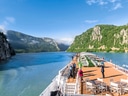 Passagierschiff auf Fluss mit bewaldeten Bergen.