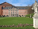 Barockpalast mit Garten und Statue im Vordergrund.