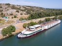 Langes Boot fährt an bewaldetem Flussufer vorbei.