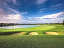 Golfplatz mit Sandbunkern und Wasserhindernis unter blauem Himmel.