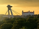 Brücke mit Aussichtsturm und Schloss bei Sonnenuntergang, umgeben von Bäumen.