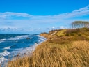 Steilküste mit Gras am Meer unter blauem Himmel.