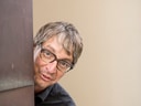Mann mit Brille schaut um die Ecke einer Wand.