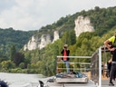 Person auf Boot fotografiert Landschaft mit weissen Klippen und grünem Wald.