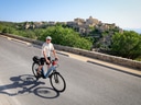 Mann auf Fahrrad vor Dorf auf Hügel.