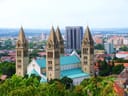 Kirche mit vier Türmen in einer Stadtlandschaft, mit Wohngebäuden und Bäumen.