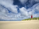 Roter Leuchtturm auf sandiger Düne unter bewölktem Himmel.