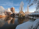 Verschneite Flusslandschaft mit Fachwerkhaus und Bäumen.