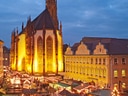 Beleuchteter Weihnachtsmarkt vor einer Kirche bei Dämmerung.