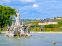 Prunkvoller Springbrunnen im Park mit Schloss und blauem Himmel.