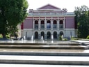 Historisches Gebäude mit Brunnen auf Vorplatz.