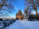Alte Backsteinkapelle im Schnee mit blauem Himmel und Bäumen.