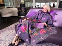 Lächelnde Person auf lila Sofa in buntem Kleid sitzend.