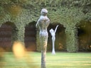Zwei Skulpturen im Garten vor einer Efeuwand.