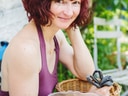 Frau mit rotem Haar sitzt im Garten mit Körbchen.