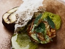 Gourmetgericht mit Schaumelementen und grüner Sauce auf einem Teller serviert.
