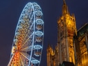 Beleuchtetes Riesenrad neben einer gotischen Kathedrale bei Nacht.