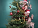Fünf Personen stehen gestapelt hinter einem weihnachtlich geschmückten Baum und winken.
