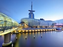 Beleuchtetes modernes Gebäude am Wasser bei Dämmerung.