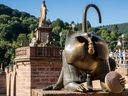 Brunnenfigur mit Spiegel auf Brücke, Statue im Hintergrund.