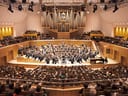 Orchester spielt in voller Konzerthalle vor Publikum.