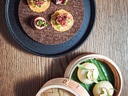 Teller mit drei kleinen Häppchen und Dampfkörbchen mit zwei gedämpften Brötchen.