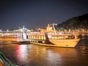 Beleuchtetes Flusskreuzfahrtschiff bei Nacht am Ufer.
