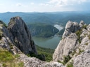Blick auf eine felsige Landschaft mit Fluss und bewaldeten Hügeln in der Ferne.