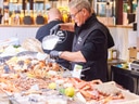 Mann hinter einer Fisch- und Meeresfrüchte-Theke auf einem Markt.