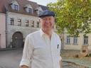 Mann mit Mütze auf einem Platz vor alten Gebäuden.
