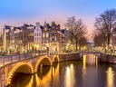 Beleuchtete Grachtenbrücke in Amsterdam bei Abenddämmerung.