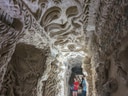 Steiniger Tunnel mit kunstvoll geschnitzten Wänden, zwei Personen im Hintergrund.