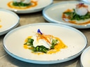 Gourmetgericht auf weissem Teller mit grünen Blättern und Sosse.