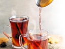Zwei Gläser Glühwein mit Orangenscheiben und Zimtstangen.