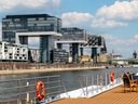 Blick von einem Boot auf moderne Architektur am Flussufer mit wolkigem Himmel.