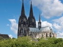 Gotische Kathedrale mit zwei Türmen hinter grünen Bäumen an einem wolkigen Tag.