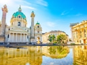 Barockkirche und Gebäude spiegeln sich in einem Wasserbecken.