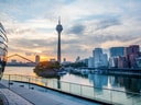 Stadtansicht mit Fernsehturm und Fluss bei Sonnenuntergang.