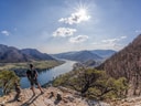 Person auf einem Felsen mit Blick auf einen Fluss und Berge bei Sonnenschein.