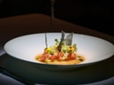 Gourmetgericht in Schale mit Weinglas im Hintergrund.