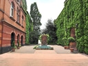 Hof mit Backsteingebäuden, grün bewachsene Wände und ein Brunnen in der Mitte.