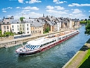 Flusskreuzfahrtschiff auf Kanal neben alten Häusern bei Sonnenschein.