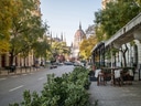 Strassenszene mit Terrasse und Bäumen, im Hintergrund ein grosses Gebäude mit Kuppel.