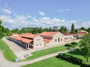 Historisches Gebäude mit roten Dächern und Steinmauern in einer grünen Umgebung.