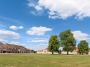 Weiträumiger Rasenbereich mit historischen Gebäuden und Bäumen bei blauem Himmel.