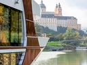 Teil eines modernen Schiffes auf einem Fluss mit einem grossen, historischen Gebäude im Hintergrund.